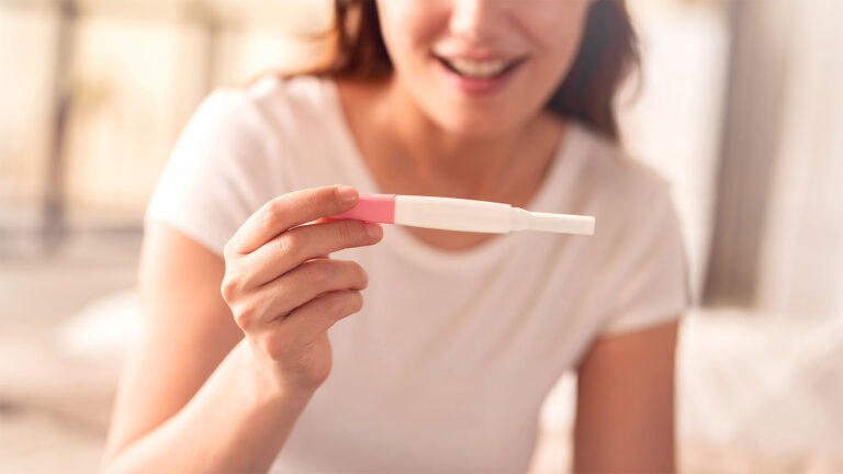 Mujer sosteniendo un test de embarazo con resultado positivo.